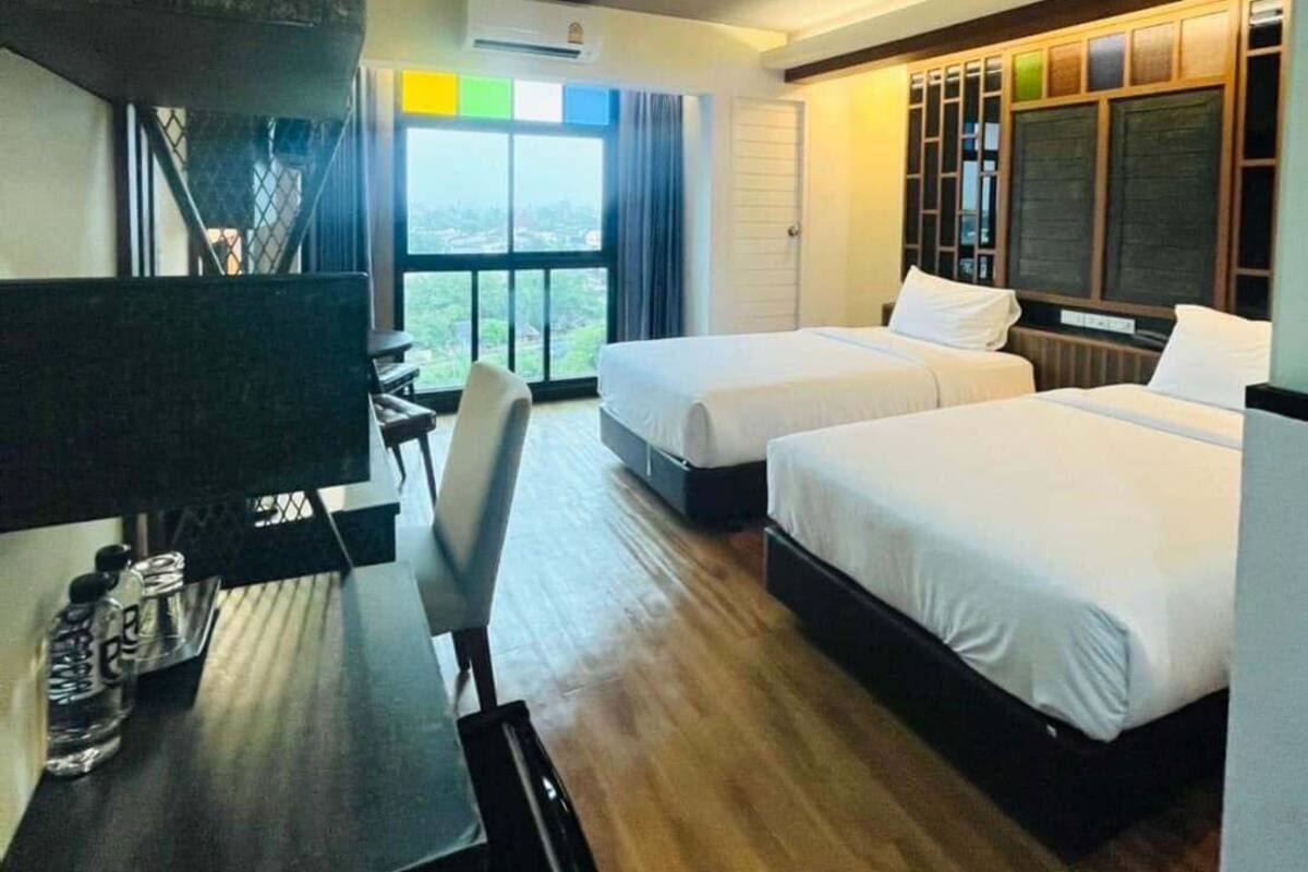 Habitación de hotel con dos camas, un escritorio, una silla y un amplio ventanal con vistas.
