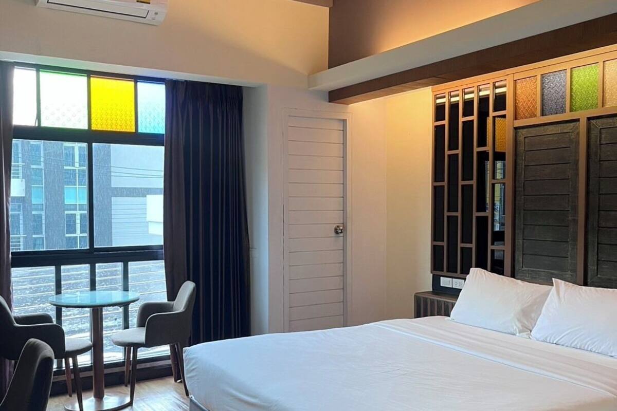 Una habitación de hotel con una cama, una mesa con sillas, una ventana con cortinas y un equipo de aire acondicionado.