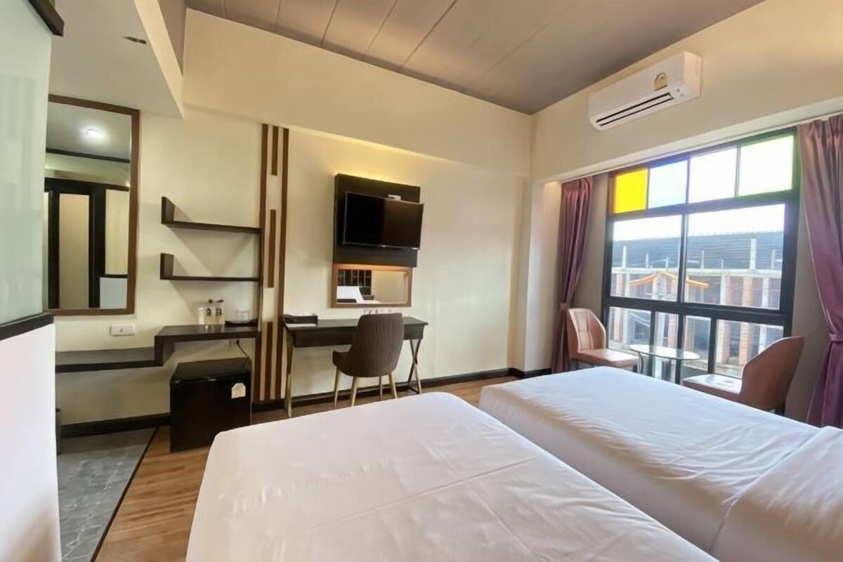Habitación de hotel con cama, escritorio, silla, televisor y ventana grande.