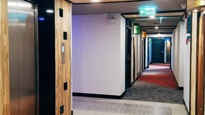 Un pasillo de hotel con paneles de madera, alfombra roja y un ascensor a la izquierda.