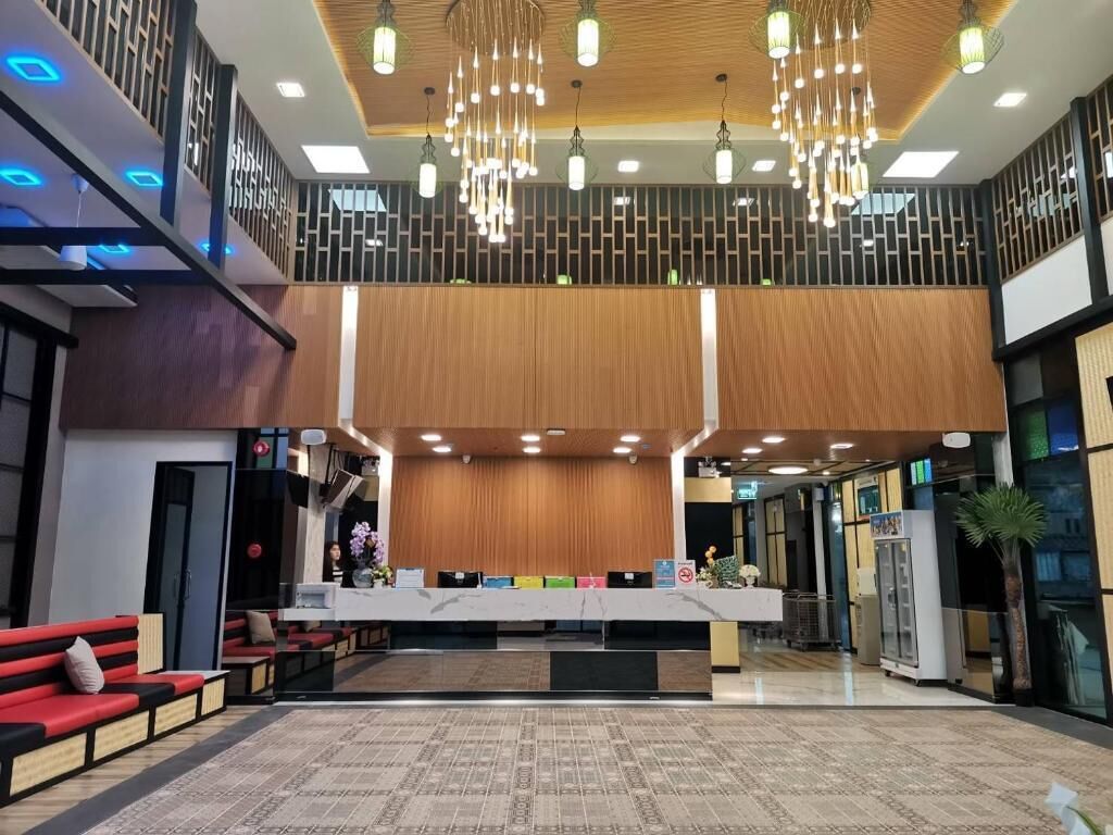 Een moderne hotellobby met een receptiebalie, een zithoek en een hoog plafond met hangende lampen.