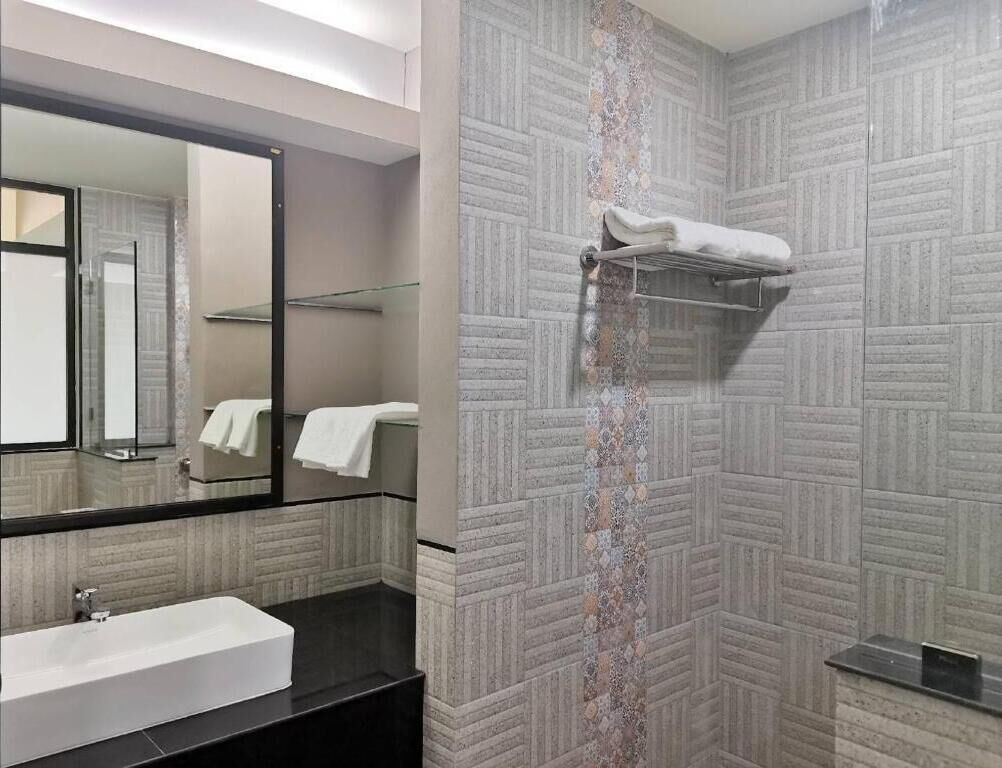 Een moderne badkamer met een grote spiegel, een witte wastafel, een handdoekhouder en behangtegels.