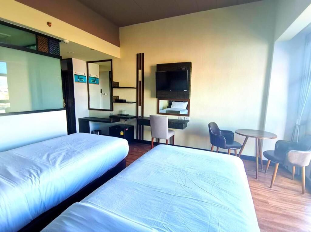 A hotel room with two beds, a desk, a TV, and a small seating area.
