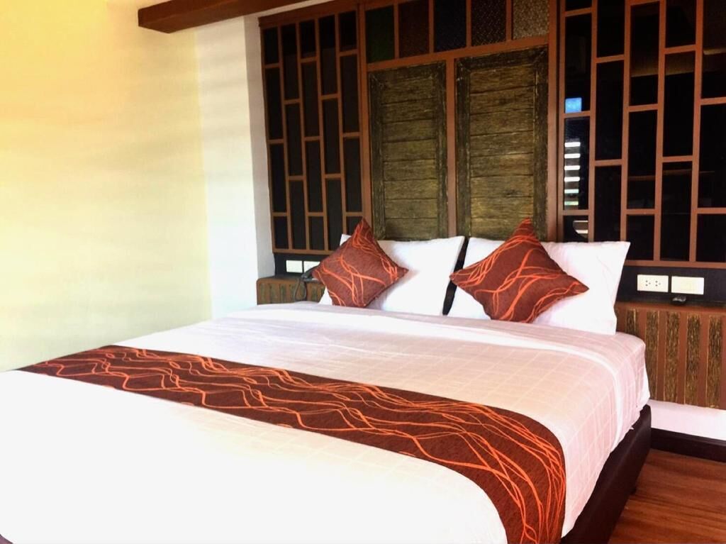 A hotel room with a large bed, wooden headboard, and a traditional Asian-style window.