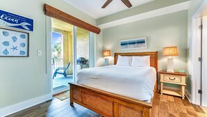 Un dormitorio con cama de madera, ventilador de techo, mesita de noche con lámpara y vistas al exterior.