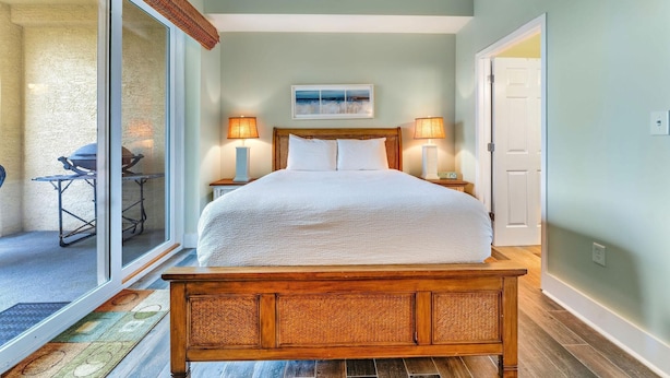 A bedroom with a large bed, two bedside lamps, a ceiling fan, and a sliding glass door leading to an outdoor area. - Summerhouse 101 - Pearl of the Gulf (Port St. Joe)