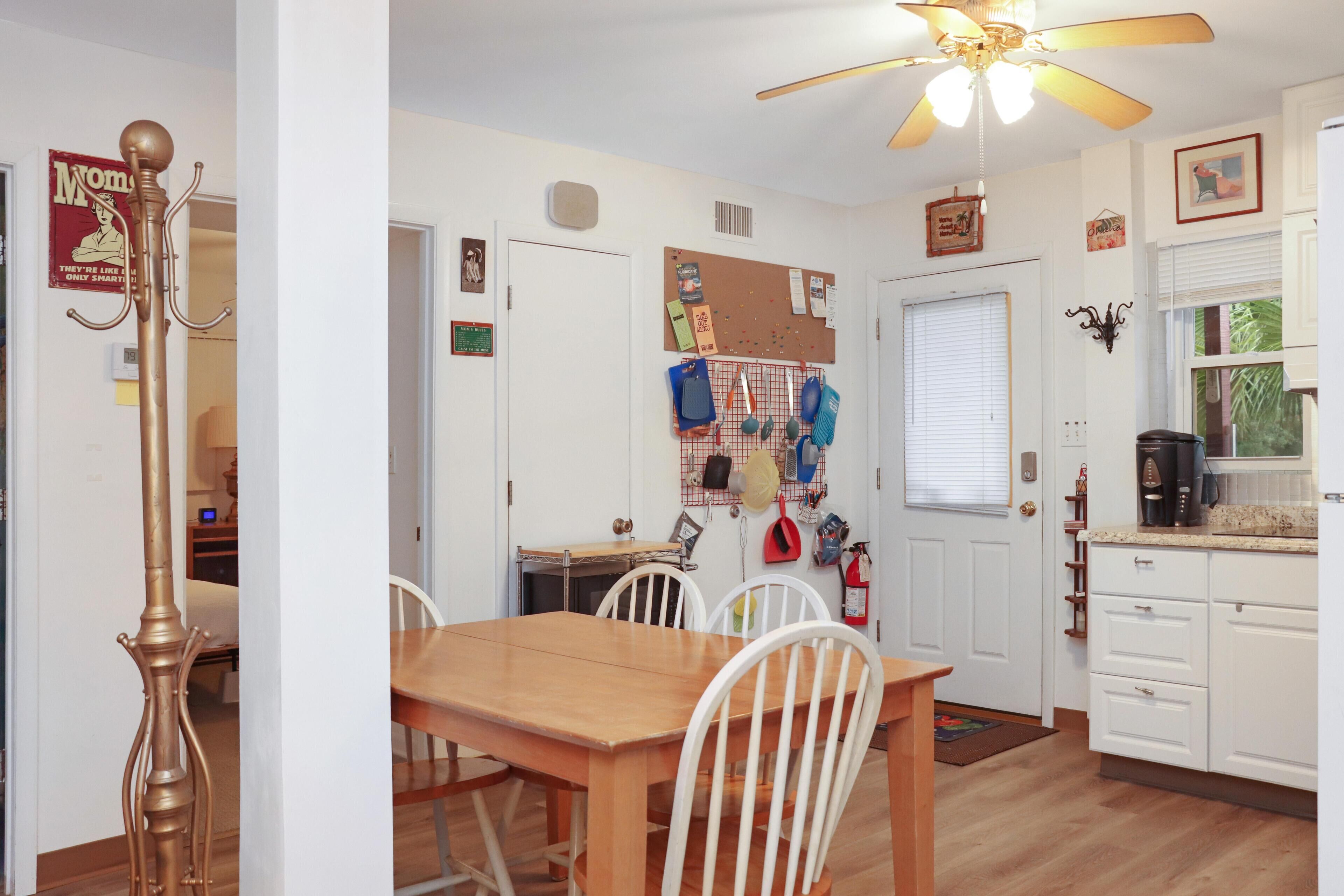 A kitchen with white cabinets, a wooden dining table, and a ceiling fan.