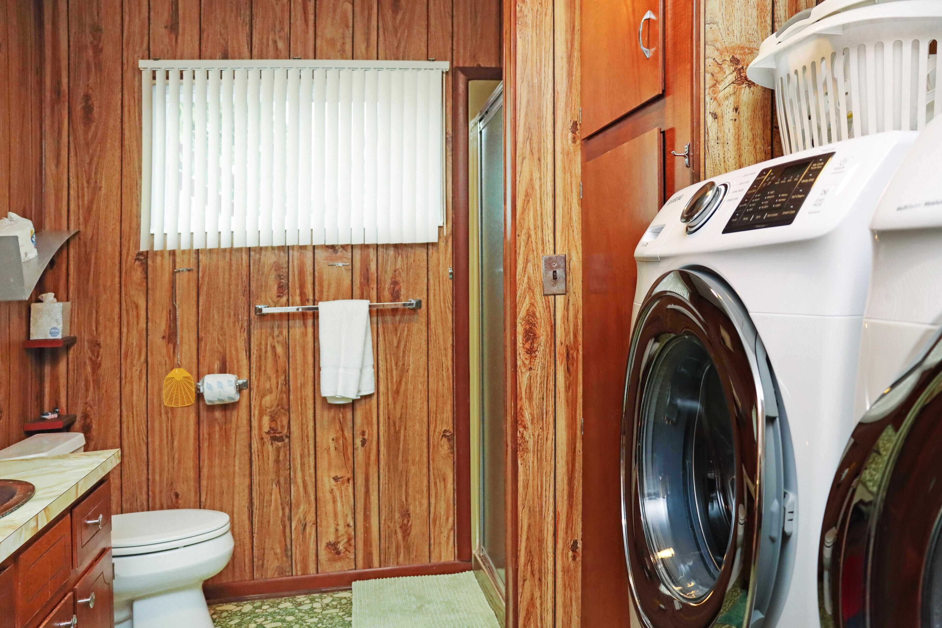 A compact bathroom with wooden walls, a toilet, a washing machine, and a window with blinds.