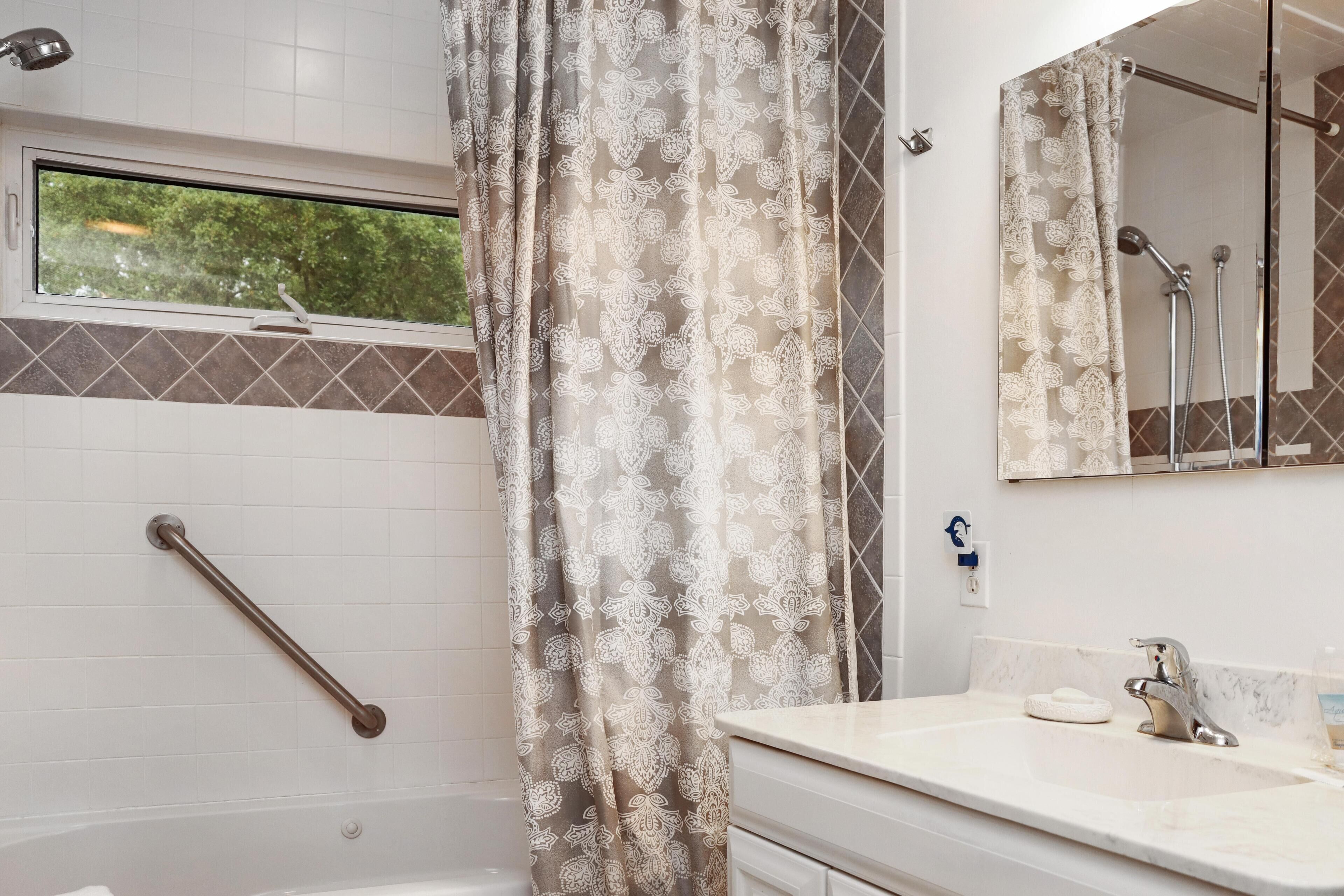 A bathroom with a shower, a handrail, a sink, and a mirror.