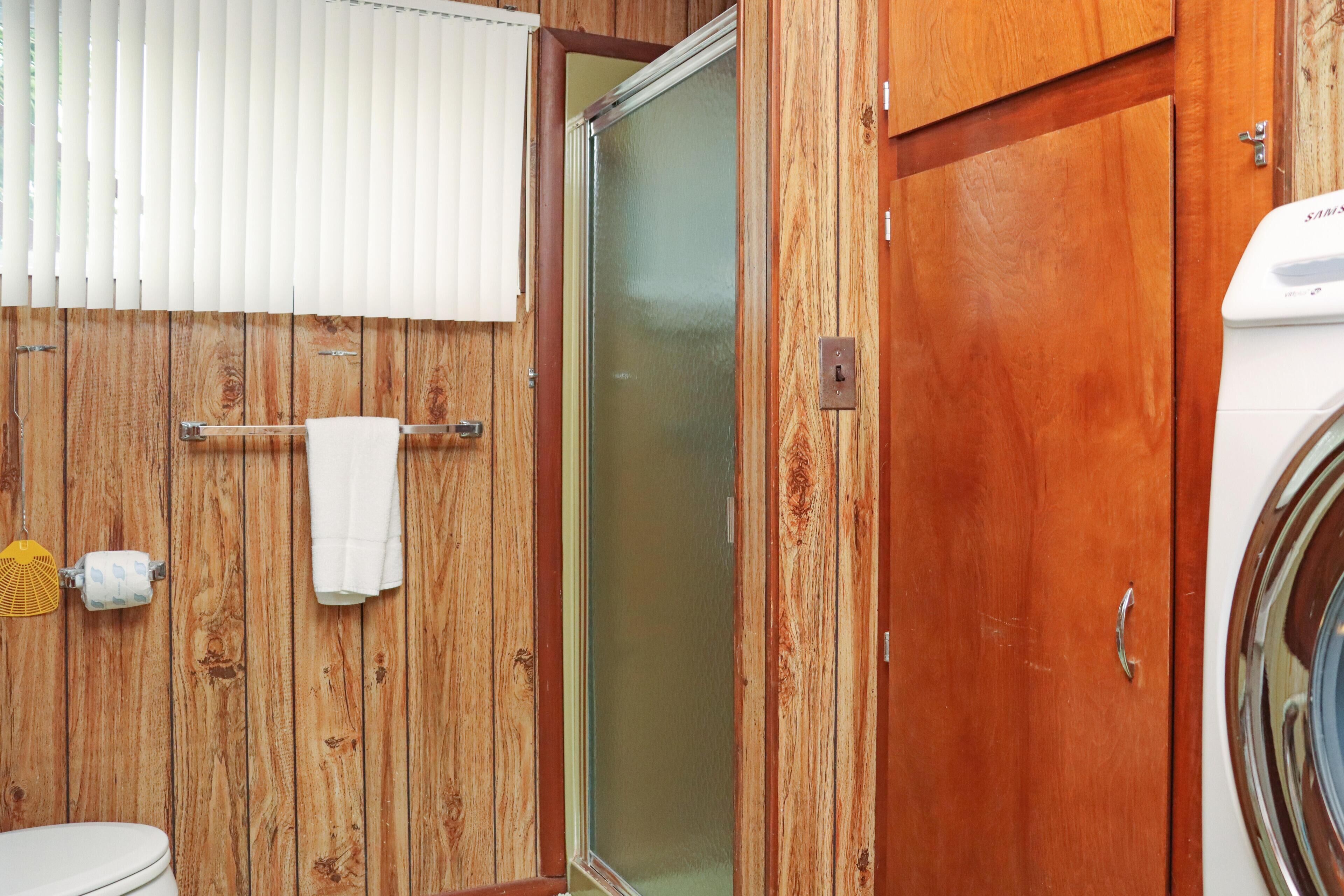 A wooden bathroom with a toilet, a towel rack, a shower, and a washing machine.