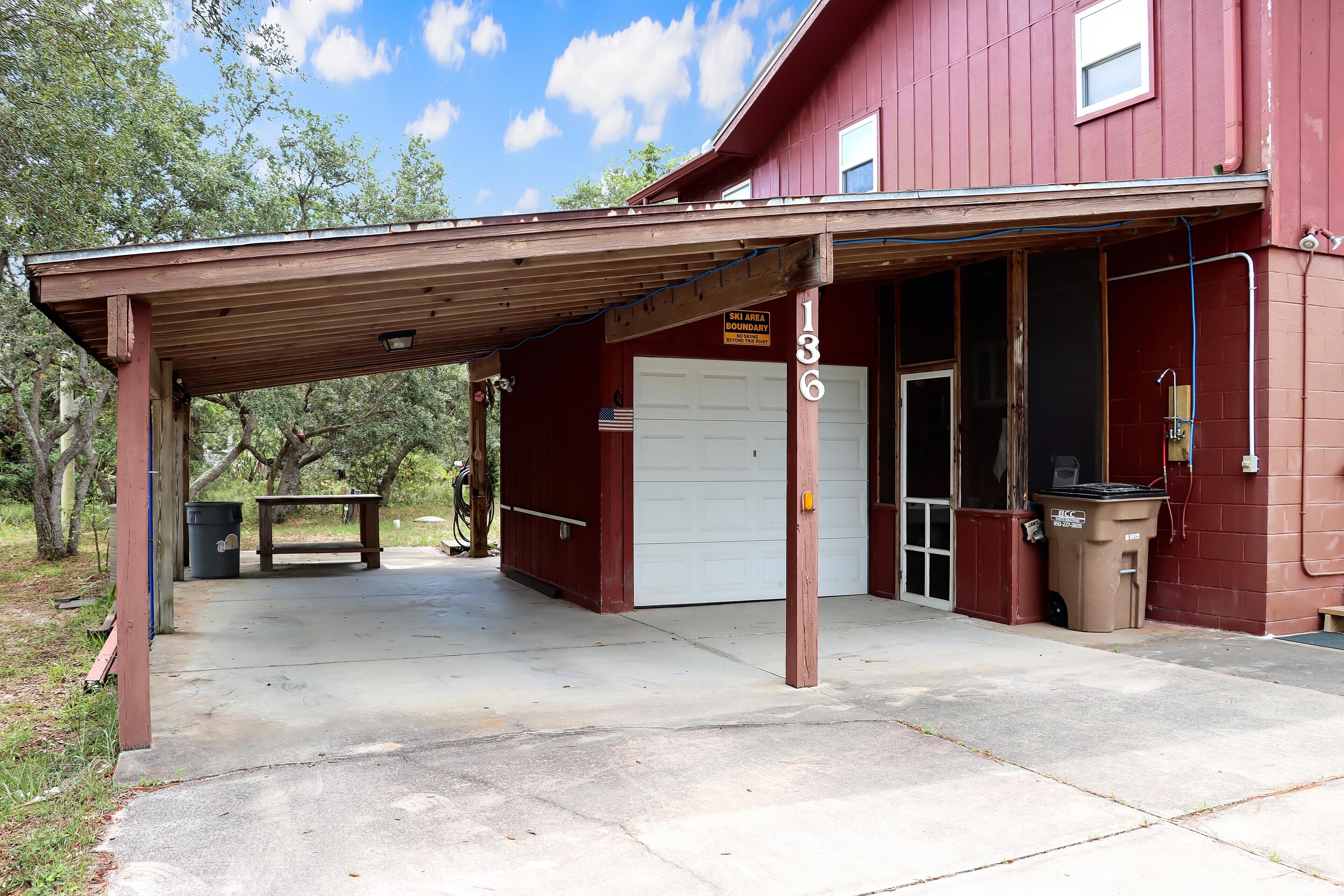 A red building with a covered parking area, a white garage door, and a trash bin.