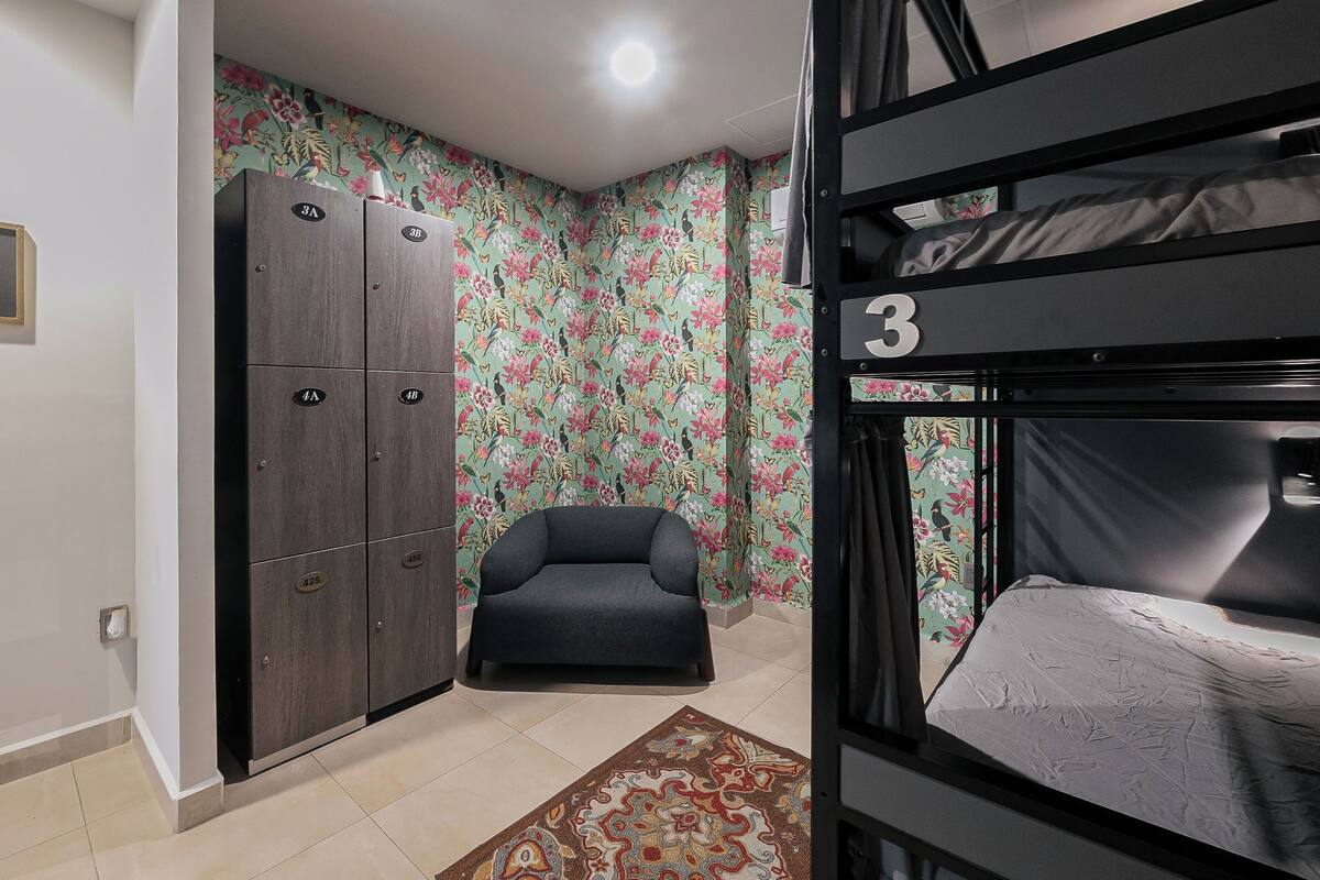 A room with a bunk bed, a sofa, a patterned rug, and a wardrobe with numbered compartments.