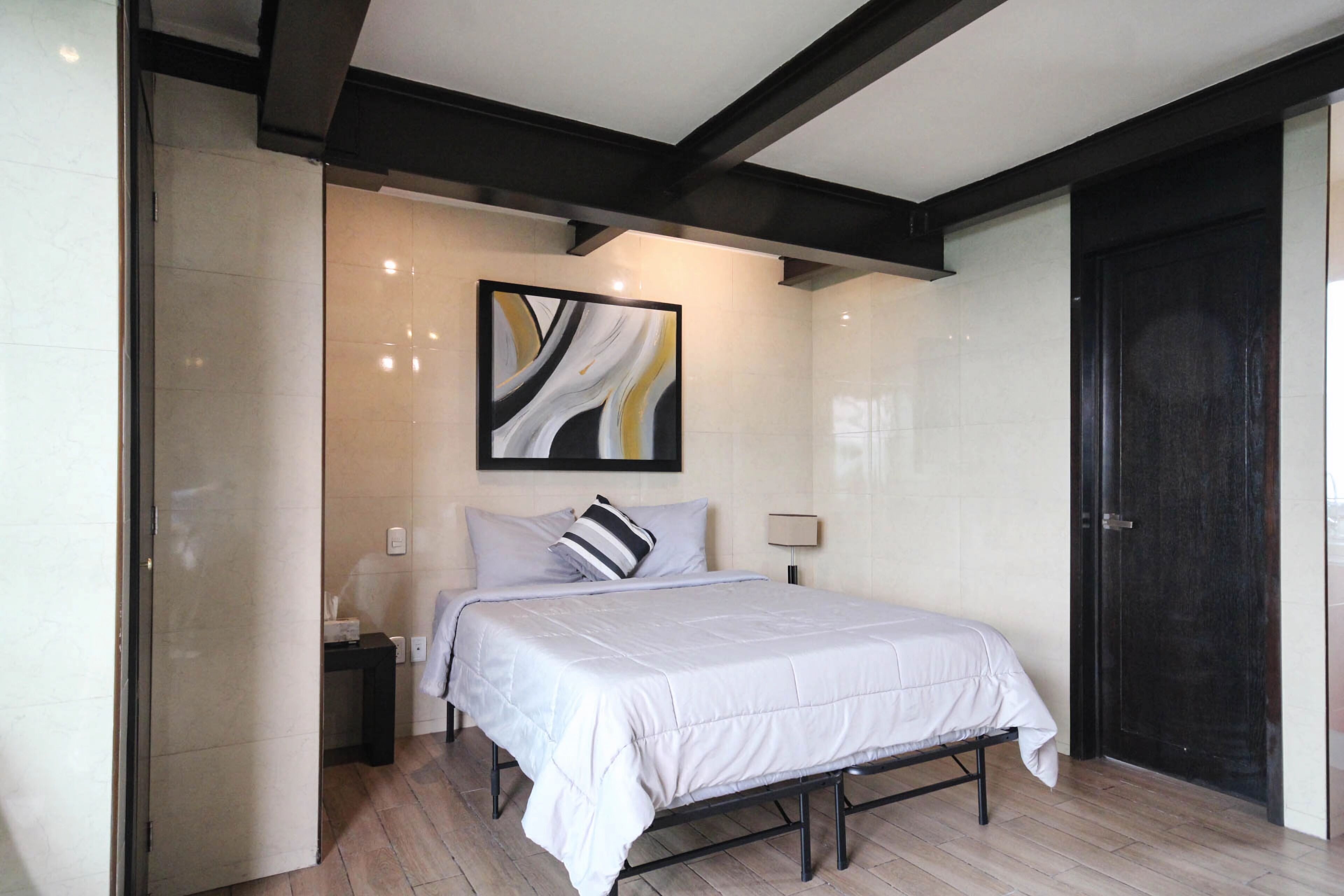 Un dormitorio moderno con cama, mesita de noche, un cuadro abstracto en la pared y una puerta oscura.