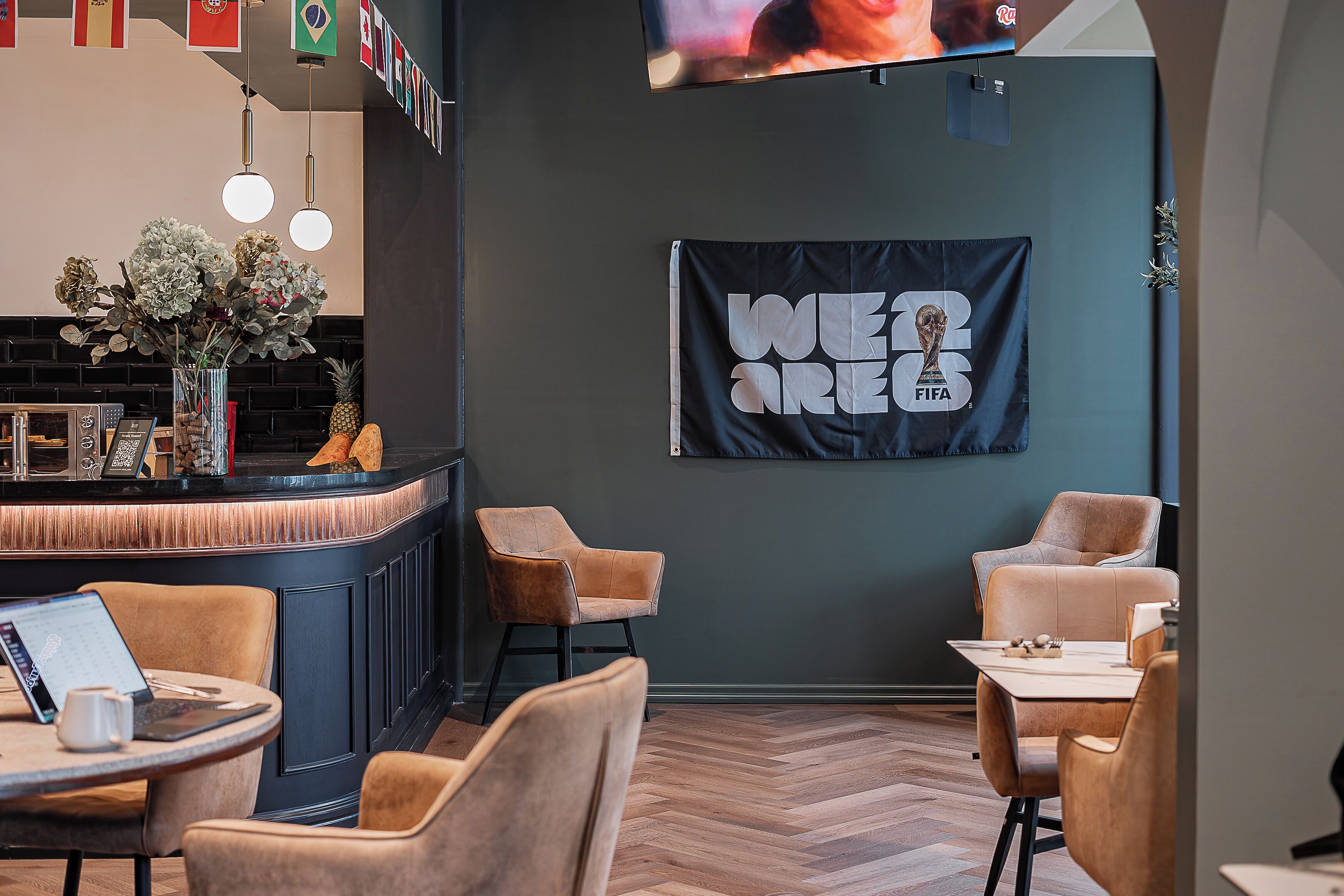 Zona de bar con pantalla de televisión, asientos con mesas e un banderín de la Copa Mundial de la FIFA.