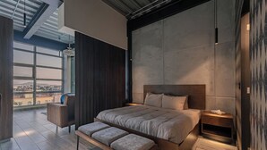 A modern bedroom with a large bed, a bench, a nightstand, and a view of the city through large windows. - Mr. Herold homes (Mexico City)