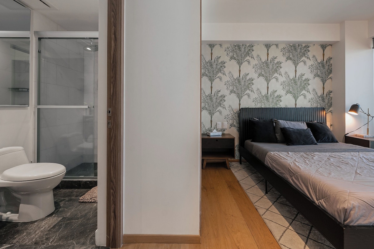 A modern bedroom with a bed, bedside tables, a nightstand, a shower, and a toilet.