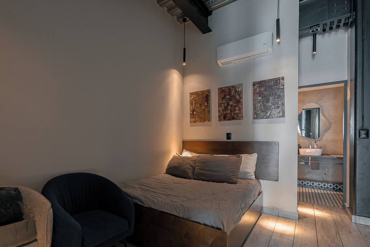 A modern bedroom with a bed, a chair, and a bathroom visible through an open door.
