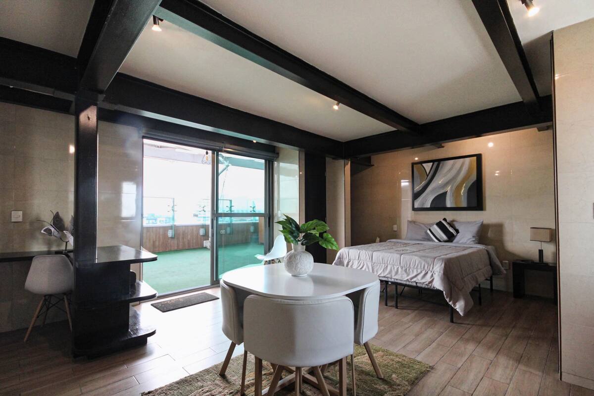 A modern bedroom with a large bed, a bedside table, a chair, and a view of a balcony.