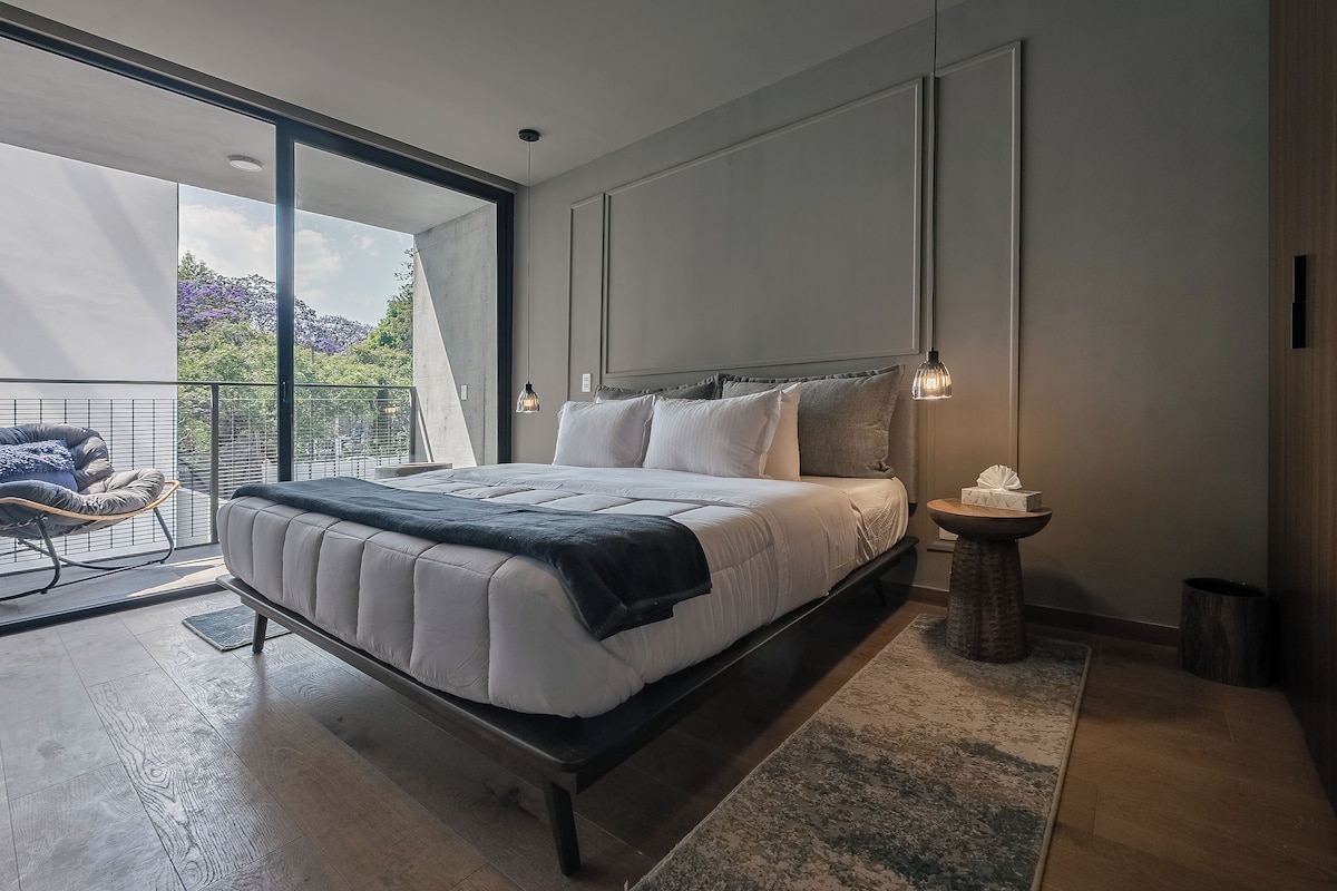 Un dormitorio moderno con una cama grande, una mesita de noche pequeña y vistas al exterior.