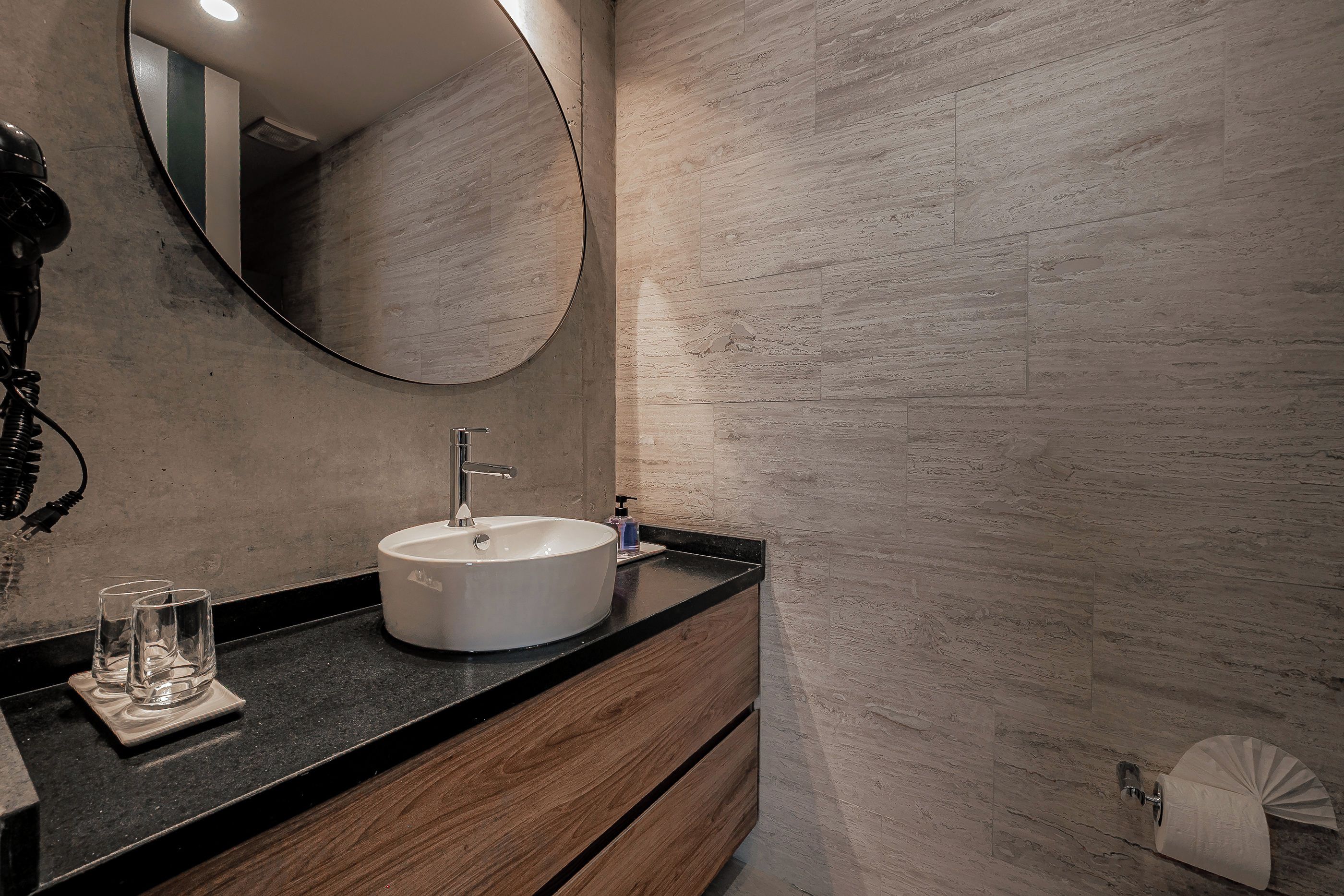 A bathroom with a round mirror, a white sink, and a wooden vanity.