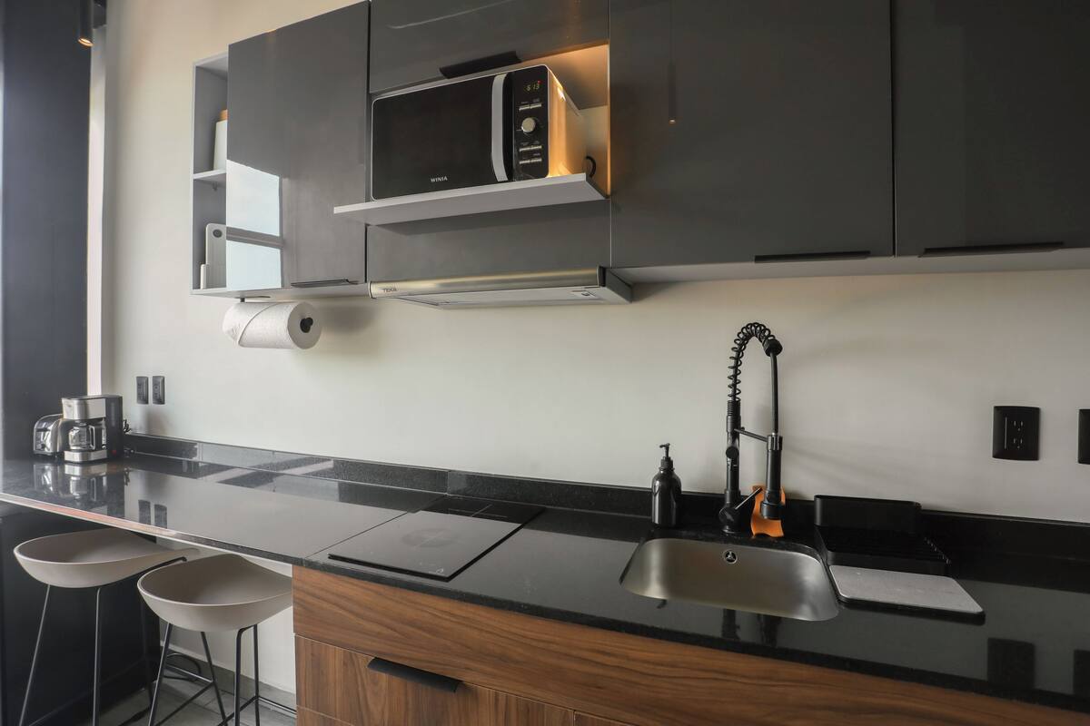 A modern kitchen with a black countertop, stainless steel sink, and a built-in microwave.