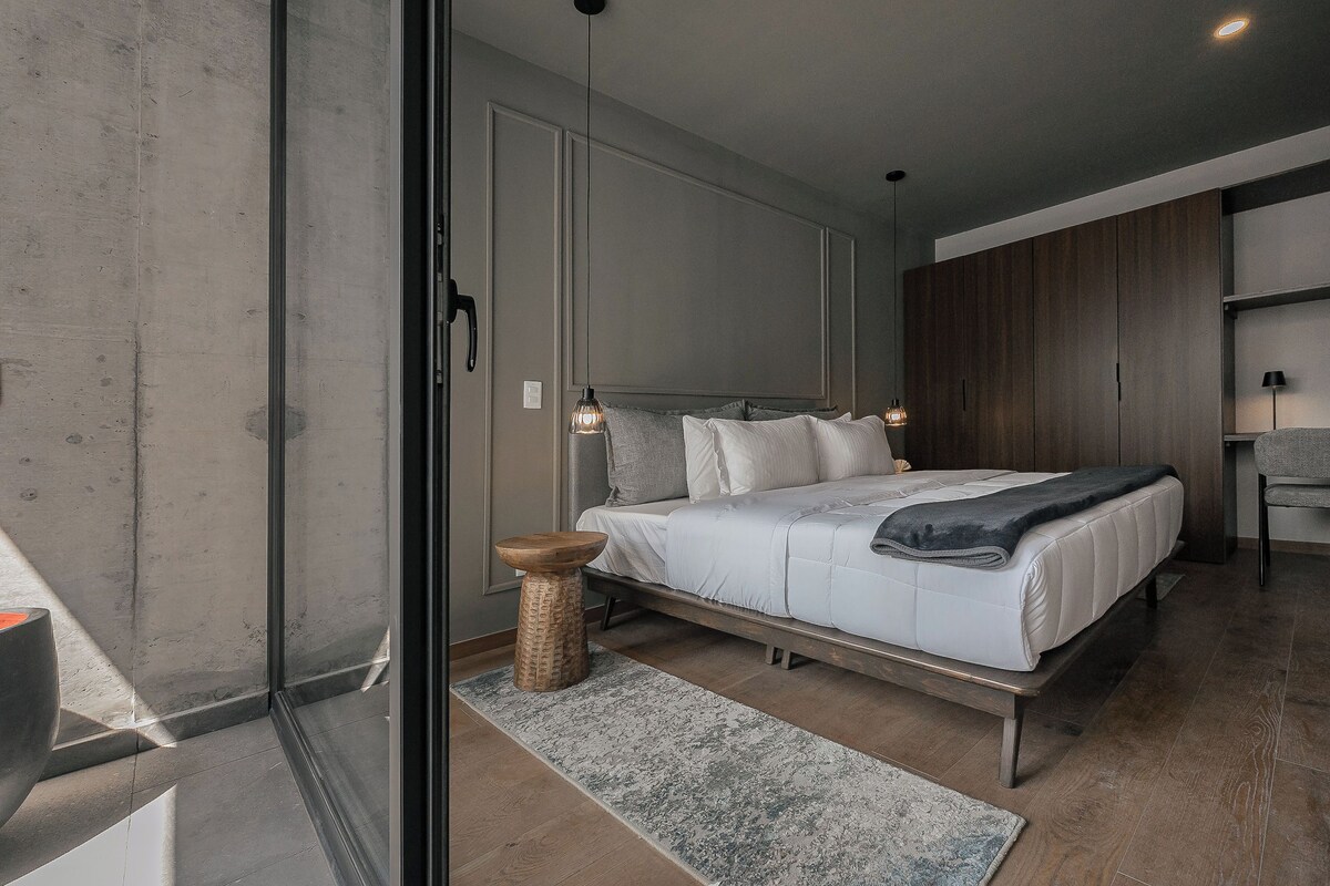 A modern bedroom with a large bed, a wooden wardrobe, and a small side table.