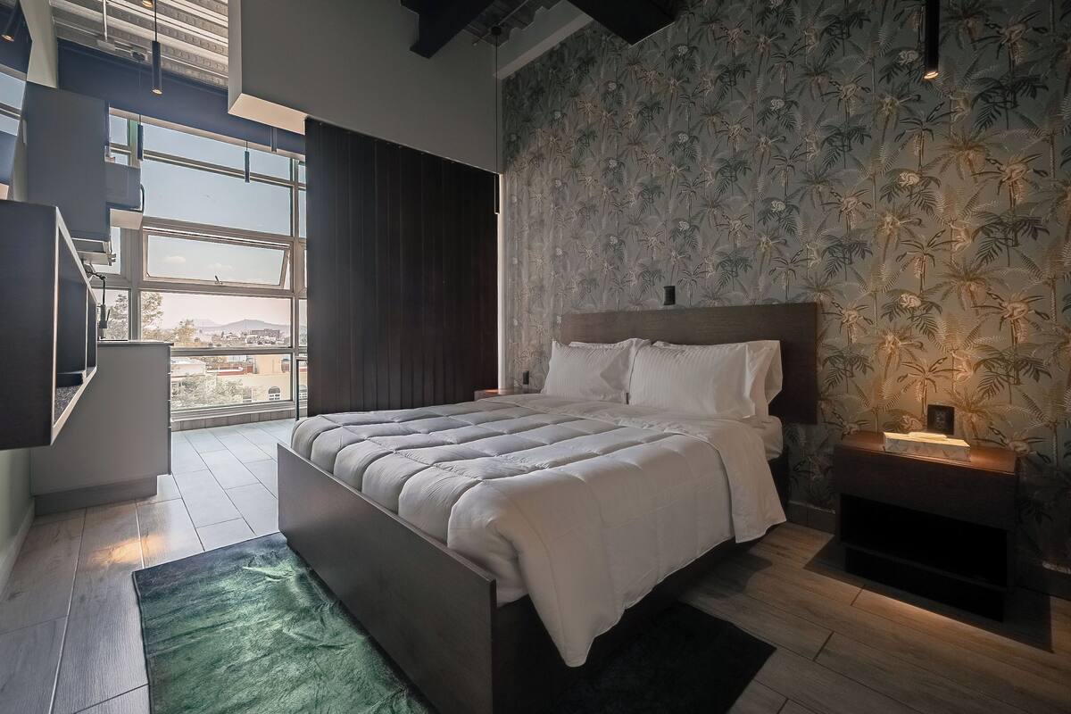 A modern bedroom with a large bed, a TV, and a view of the outdoors.