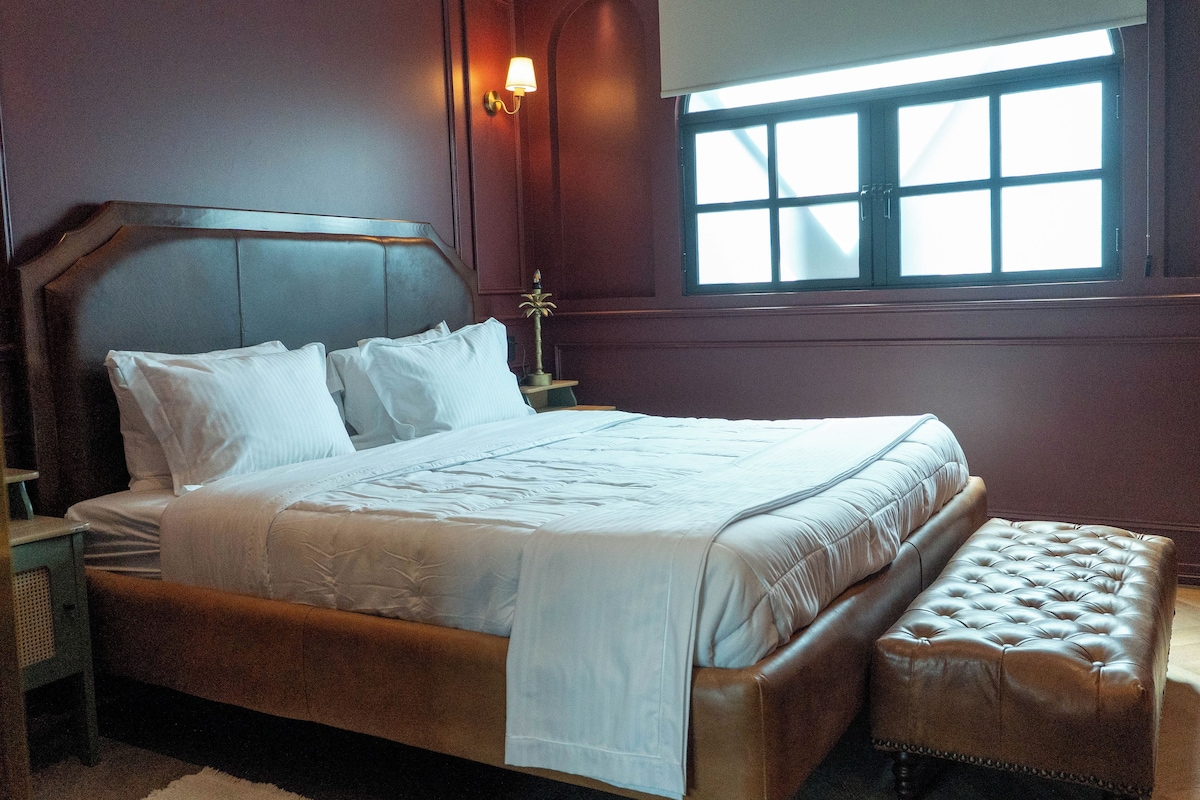 A bedroom with a large bed, a bedside table, a lamp, and a window.