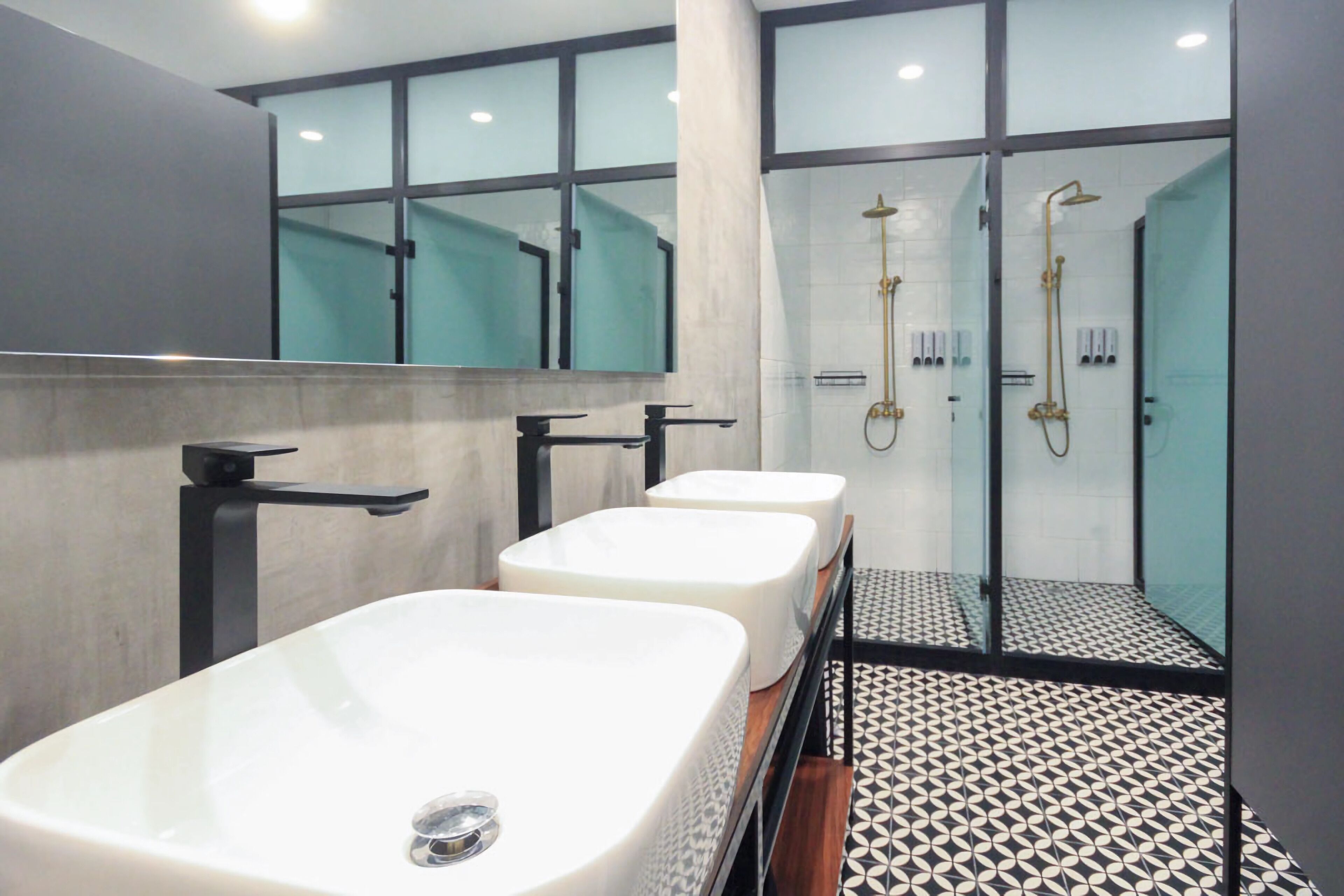 A modern bathroom with three white sinks, a large mirror, and a glass-enclosed shower area.