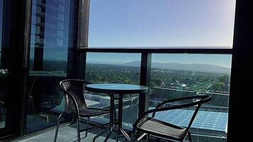 A balcony with two chairs and a table, overlooking a cityscape with buildings and a clear sky.
