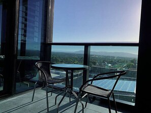 A balcony with two chairs and a table, overlooking a cityscape with buildings and a clear sky. - SkyGarden Luxury Apt | Mountain & Sunrise Views (Glen Waverley)