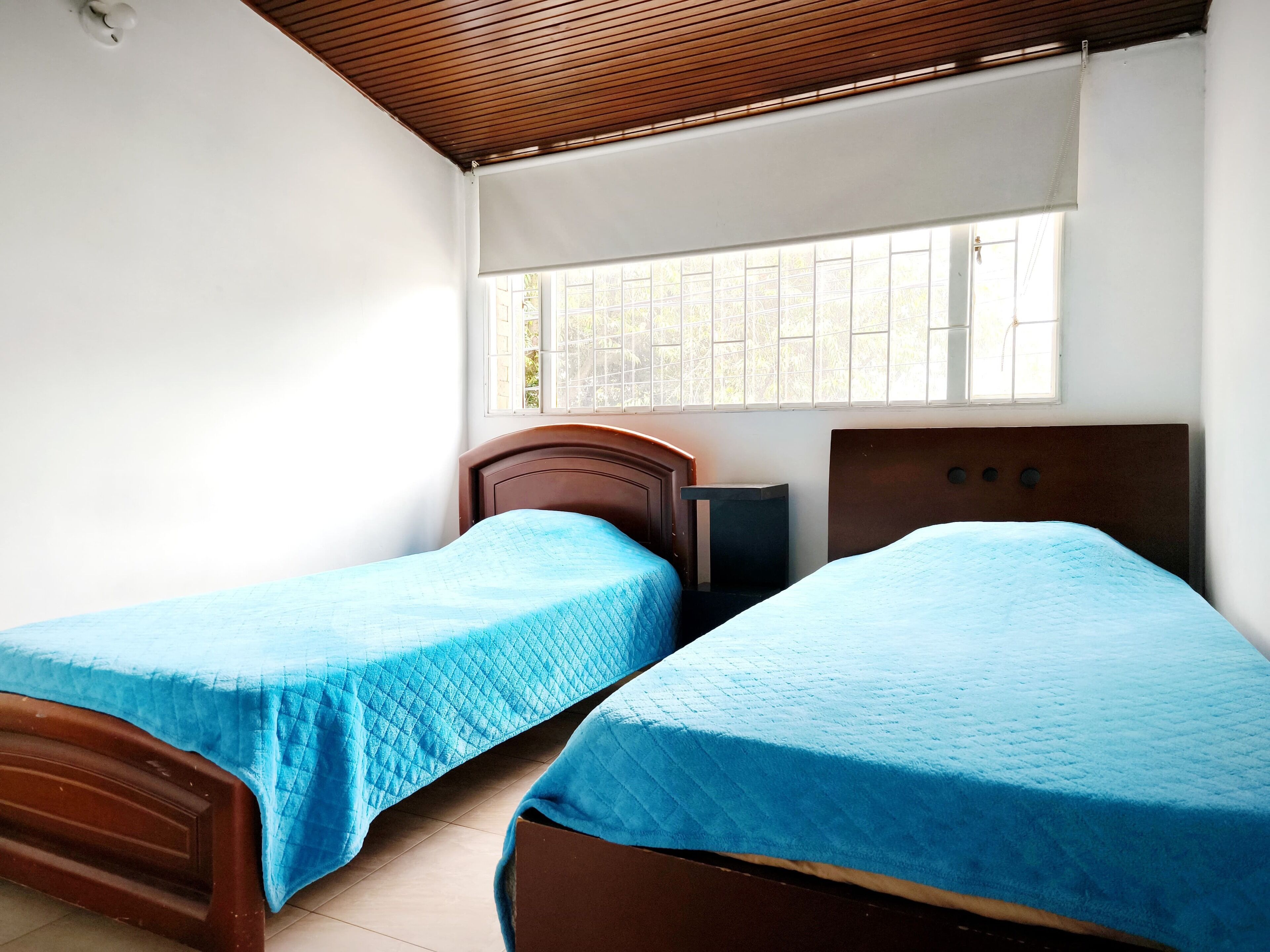 A room with two beds, a window with bars, and a wooden ceiling.