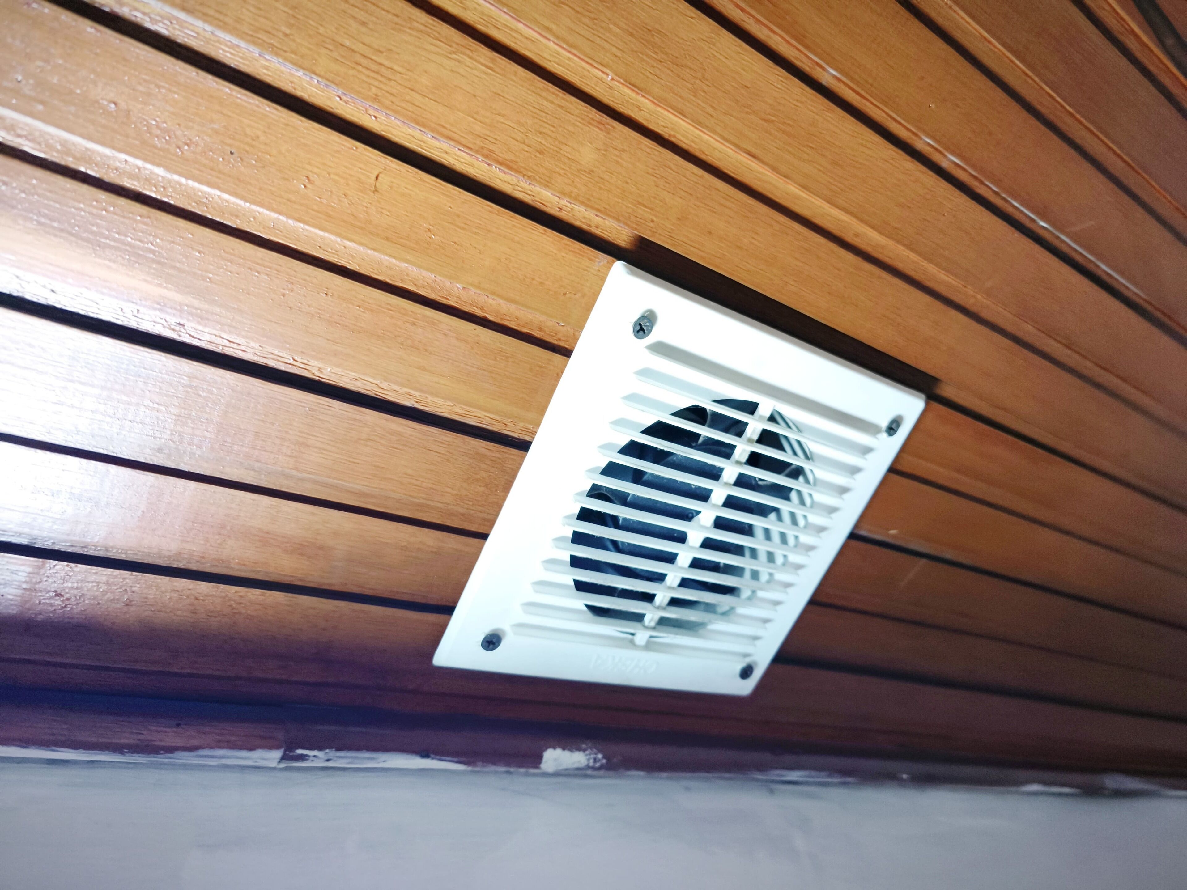 A ceiling vent in a room with wooden paneling.