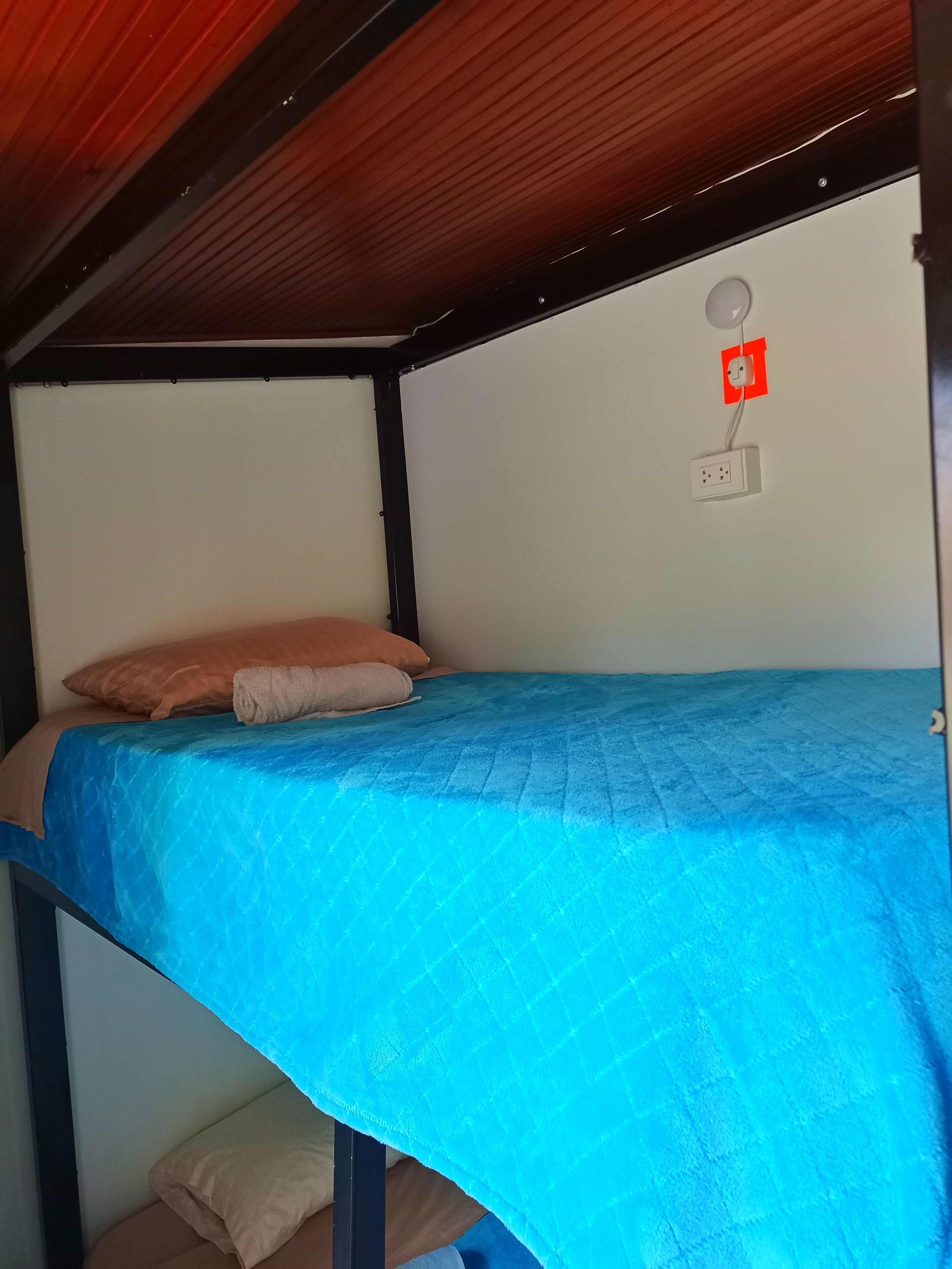 A bunk bed with a blue mattress and a single orange pillow.