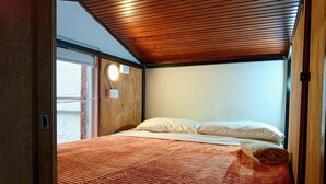 Un dormitorio con techo de madera, una cama con ropa blanca y una lámpara de pared.