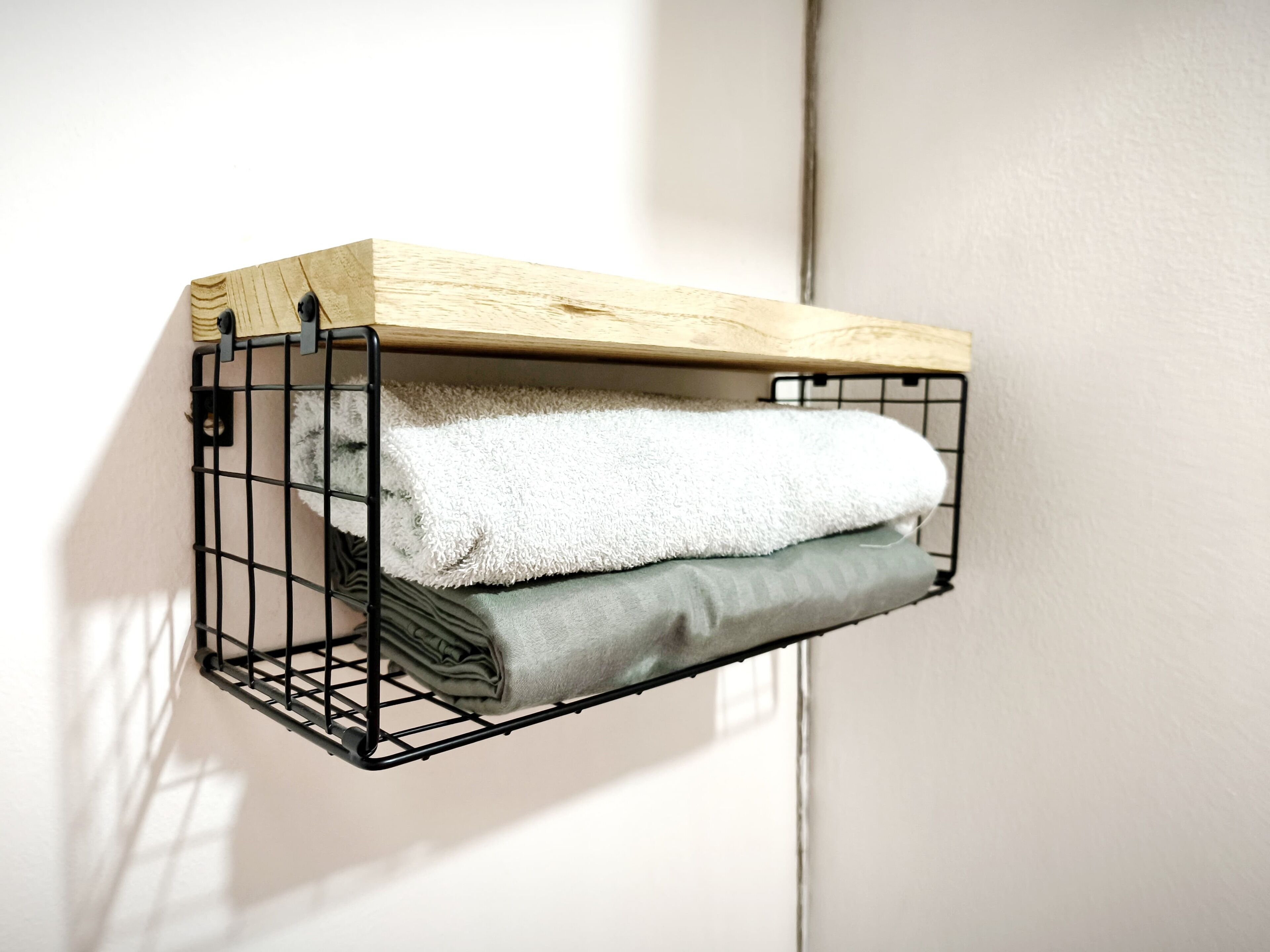 A black metal wire shelf with a wooden top, holding folded towels.