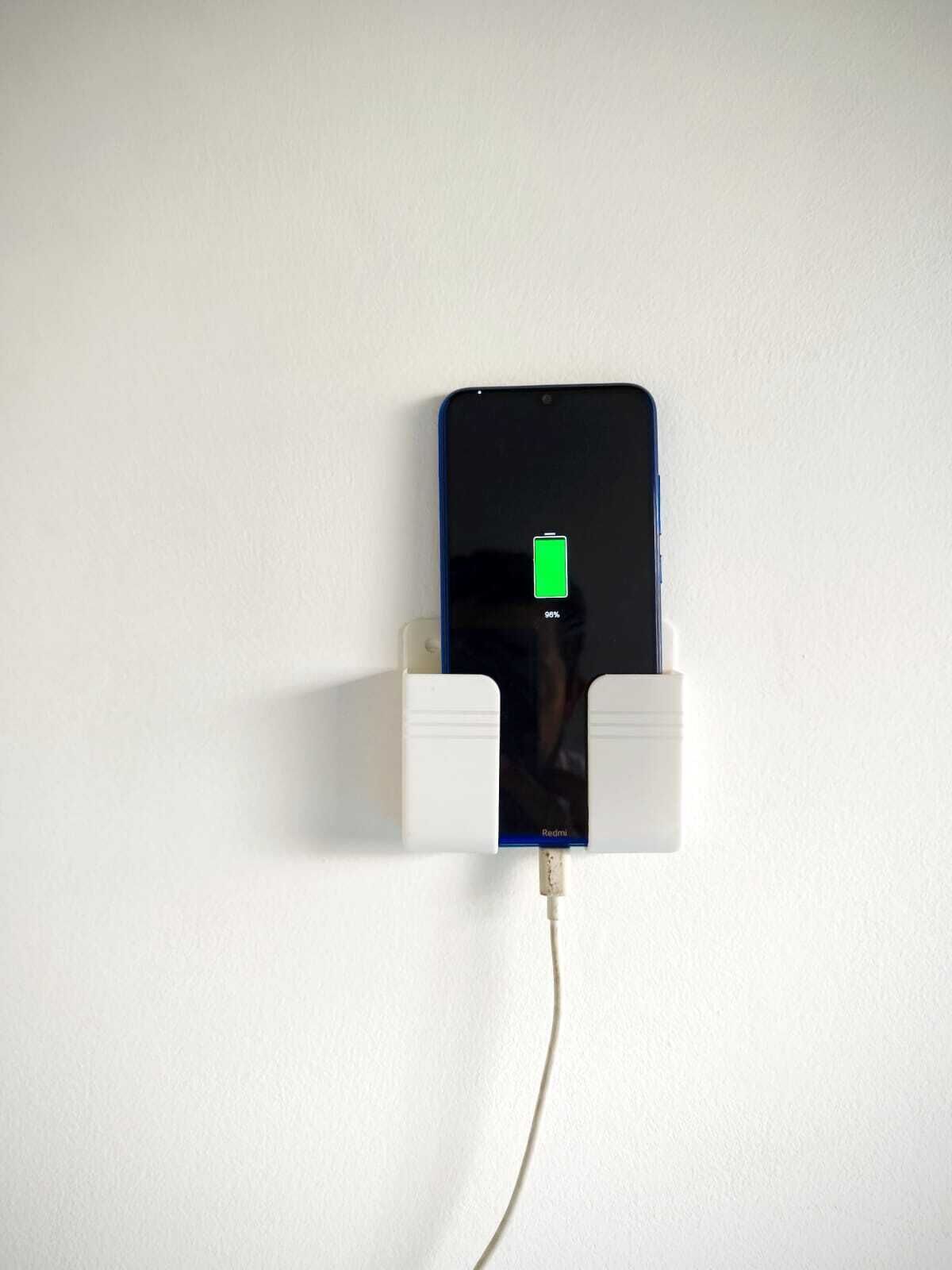 A smartphone charging on a white wall-mounted charging station.