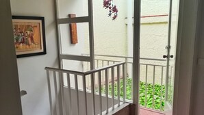 Habitación con techo de madera, barandal blanco, un cuadro en la pared y vistas al exterior con vegetación.
