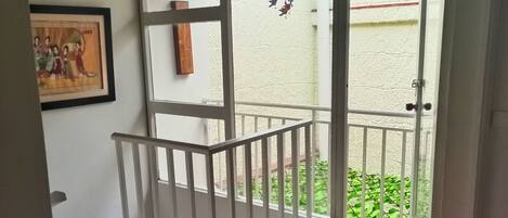 A room with a wooden ceiling, a white railing, a framed picture on the wall, and a view of greenery outside.