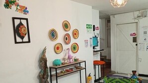 Un salón moderno con una pared blanca, una consola, un sillón tejido colorido y una lámpara en el techo.