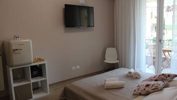 Ein Hotelzimmer mit Bett, Wandfernseher, Minibar, Stuhl und Balkon mit Gartenmöbeln.