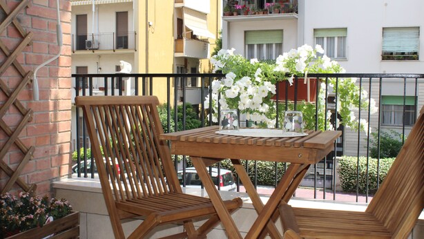 Une table et des chaises en bois sur un balcon donnant sur un immeuble à plusieurs étages.