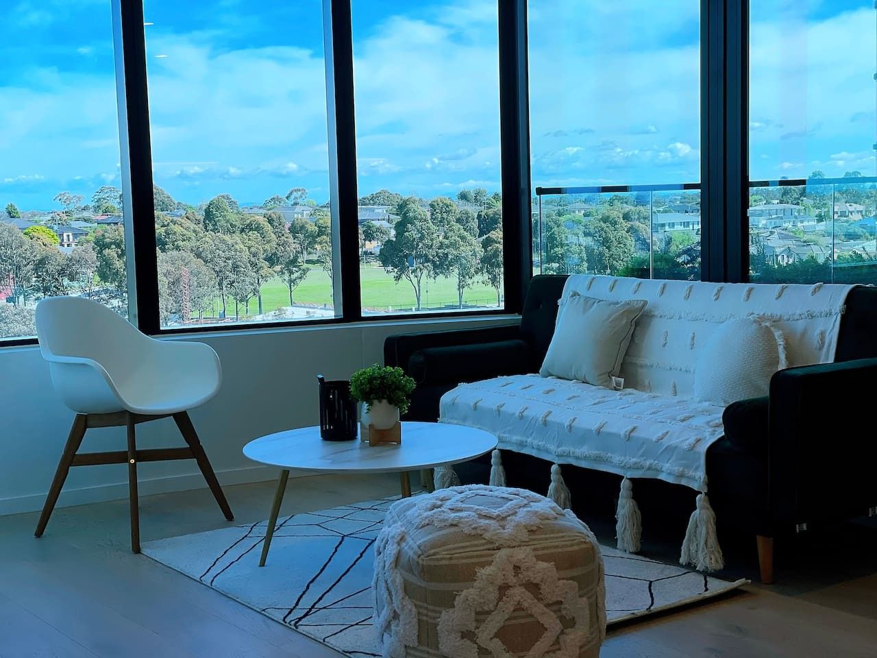 A modern living room with a sofa, a chair, a small table, and a view of a green landscape through large windows.