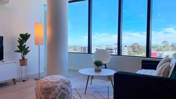 A modern living room with a large window, a flat-screen TV, a round coffee table, and a comfortable sofa.