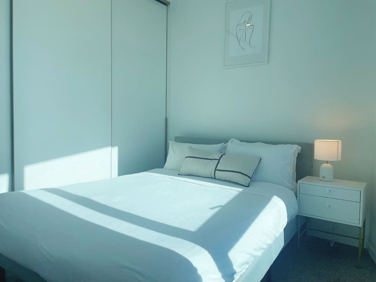 A bedroom with a bed, nightstand, and wall-mounted artwork.