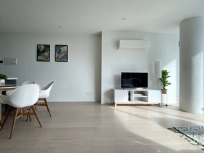 Un salon moderne comprenant un coin repas, un téléviseur à écran plat et un meuble de rangement blanc pour les appareils multimédias.