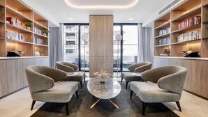A modern library with bookshelves, comfortable seating, and a central column. - Panoramic Views! Spacious 2 Bed, 2 Bath Luxury Apartment w/ Free Parking (Glen Waverley)
