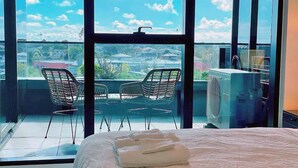 A hotel room with a large window, a bed with neatly folded towels, and two chairs outside. - Panoramic Views! Spacious 2 Bed, 2 Bath Luxury Apartment w/ Free Parking (Glen Waverley)