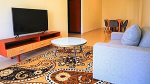 Uma sala de estar com televisão de tela plana, sofá, mesa de centro e tapete estampado.