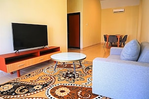 Una sala de estar con una televisión de pantalla plana, un sofá, una mesa de centro y una alfombra estampada.